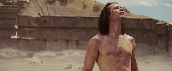 Movie still from “John Carter” (2012), directed by Andrew Stanton – A man with long hair and no shirt standing in the sand; Medium shot, Low angle