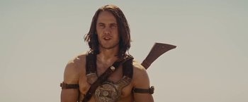 Movie still from “John Carter” (2012), directed by Andrew Stanton – A man with long brown hair holding an axe; Medium shot, Low angle