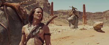 Movie still from “John Carter” (2012), directed by Andrew Stanton – A man with long brown hair is holding a spear; Medium shot, Over the shoulder angle