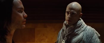 Movie still from “John Carter” (2012), directed by Andrew Stanton – A bald man wearing a scarf standing next to a wall; Close Up shot, Low angle