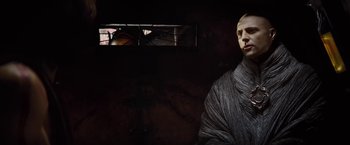 Movie still from “John Carter” (2012), directed by Andrew Stanton – A bald man in a gray robe in front of a stained glass window; Close Up shot, Low angle