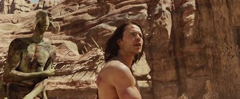 Movie still from “John Carter” (2012), directed by Andrew Stanton – A man with long black hair is standing in front of a rock wall; Medium shot, Low angle