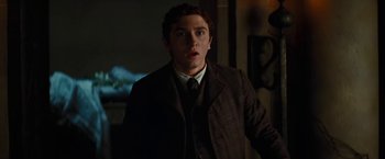 Movie still from “John Carter” (2012), directed by Andrew Stanton – A man in a suit and tie standing in front of a wall; Medium shot, Low angle