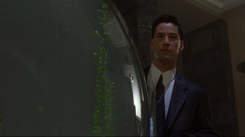 Movie still from “Johnny Mnemonic” (1995), directed by Robert Longo – A man wearing a suit and tie standing in front of a mirror; Medium shot, Low angle