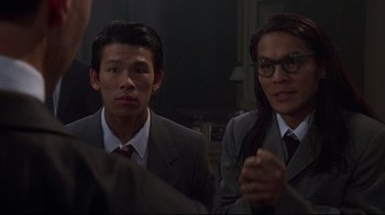 Movie still from “Johnny Mnemonic” (1995), directed by Robert Longo – A man and a woman in business suits are sitting in front of another man; Close Up shot, Over the shoulder angle