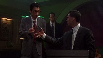 Movie still from “Johnny Mnemonic” (1995), directed by Robert Longo – A man in a suit and tie holding a cell phone; Medium shot, Over the shoulder angle