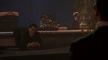 Movie still from “Johnny Mnemonic” (1995), directed by Robert Longo – A man sitting at a table in front of a window at night; Wide shot, Over the shoulder angle