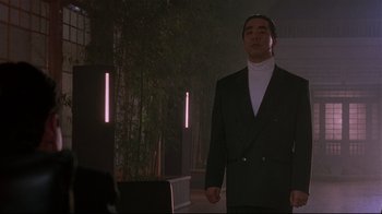 Movie still from “Johnny Mnemonic” (1995), directed by Robert Longo – A man wearing a suit and tie standing in front of trees; Medium shot, Low angle