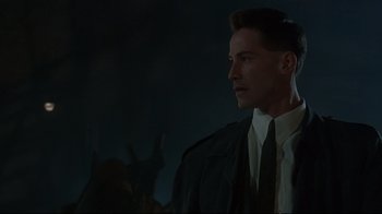 Movie still from “Johnny Mnemonic” (1995), directed by Robert Longo – A man wearing a suit and tie in a dark room; Close Up shot, Low angle