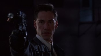 Movie still from “Johnny Mnemonic” (1995), directed by Robert Longo – A man in a suit and tie standing in the dark; Close Up shot, Low angle