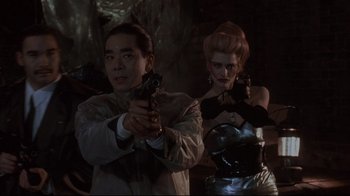 Movie still from “Johnny Mnemonic” (1995), directed by Robert Longo – A man and a woman holding guns in a dark room; Medium shot, Low angle