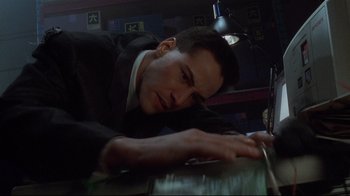 Movie still from “Johnny Mnemonic” (1995), directed by Robert Longo – A man in a black suit is leaning on a table; Close Up shot, Low angle