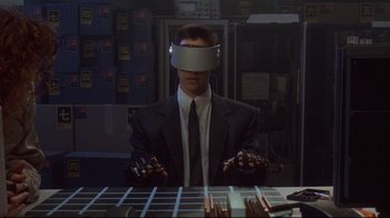 Movie still from “Johnny Mnemonic” (1995), directed by Robert Longo – A man in a suit and tie wearing a vr headset; Medium shot, High angle