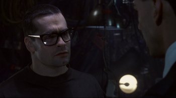 Movie still from “Johnny Mnemonic” (1995), directed by Robert Longo – A man wearing glasses and a black shirt is in a dark room; Close Up shot, Over the shoulder angle