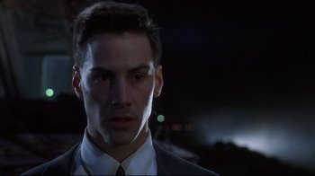Movie still from “Johnny Mnemonic” (1995), directed by Robert Longo – A person wearing a suit and tie; Close Up shot, Over the shoulder angle