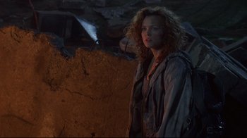 Movie still from “Johnny Mnemonic” (1995), directed by Robert Longo – A woman standing in front of a stone wall at night; Medium shot, Over the shoulder angle