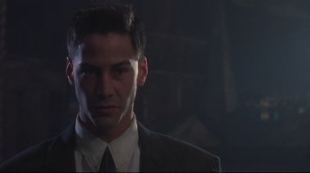 Movie still from “Johnny Mnemonic” (1995), directed by Robert Longo – A man wearing a suit and tie standing in a dark room; Close Up shot, Low angle