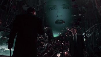 Movie still from “Johnny Mnemonic” (1995), directed by Robert Longo – Two men standing in front of a projection of a woman's face on a wall; Medium shot, Low angle