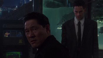 Movie still from “Johnny Mnemonic” (1995), directed by Robert Longo – A man in a suit and tie standing next to another man in a suit and tie; Medium shot, Over the shoulder angle