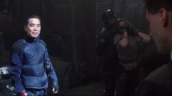 Movie still from “Johnny Mnemonic” (1995), directed by Robert Longo – A group of people standing next to each other in a room; Medium shot, Over the shoulder angle