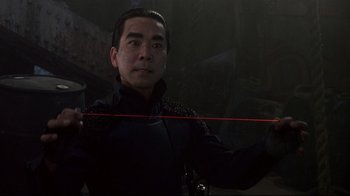 Movie still from “Johnny Mnemonic” (1995), directed by Robert Longo – A man holding a red string in a dark room; Close Up shot, High angle