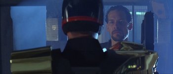 Movie still from “Judge Dredd” (1995), directed by Danny Cannon – A man looking into a mirror while a man in a motorcycle helmet looks on; Close Up shot, Low angle