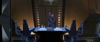 Movie still from “Judge Dredd” (1995), directed by Danny Cannon – A man sitting at a table in front of a door; Wide shot, High angle