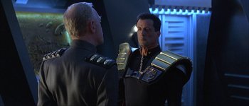 Movie still from “Judge Dredd” (1995), directed by Danny Cannon – A man in a uniform talking to another man in a uniform; Medium shot, Over the shoulder angle