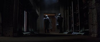 Movie still from “Judge Dredd” (1995), directed by Danny Cannon – Two people standing next to each other in a dark room; Wide shot, Low angle