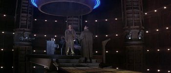 Movie still from “Judge Dredd” (1995), directed by Danny Cannon – Two people standing on steps in a dark room; Wide shot, High angle