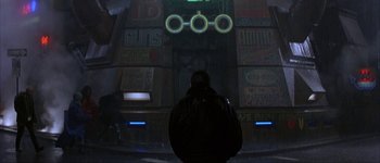 Movie still from “Judge Dredd” (1995), directed by Danny Cannon – A man standing in front of a building with neon lights; Wide shot, Over the shoulder angle