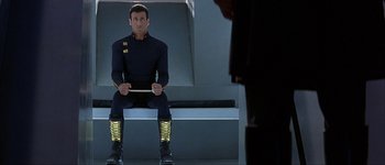 Movie still from “Judge Dredd” (1995), directed by Danny Cannon – A man sitting on top of a bench holding a stick; Medium shot, High angle