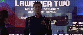 Movie still from “Judge Dredd” (1995), directed by Danny Cannon – A man in a military uniform standing in front of a screen; Medium shot, Low angle