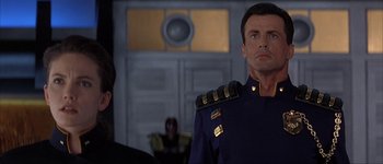 Movie still from “Judge Dredd” (1995), directed by Danny Cannon – A man in a uniform standing next to another man in a suit; Close Up shot, Low angle