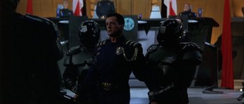 Movie still from “Judge Dredd” (1995), directed by Danny Cannon – A man in a uniform standing next to two other men in helmets; Medium shot, Low angle