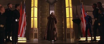Movie still from “Judge Dredd” (1995), directed by Danny Cannon – A woman in a long coat standing in front of a door; Wide shot, Low angle