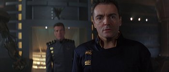 Movie still from “Judge Dredd” (1995), directed by Danny Cannon – A man in a black uniform standing next to another man in a black uniform; Close Up shot, Over the shoulder angle