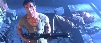 Movie still from “Judge Dredd” (1995), directed by Danny Cannon – A man holding a gun while standing next to another man laying on the ground; Medium shot, Low angle