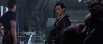 Movie still from “Judge Dredd” (1995), directed by Danny Cannon – A woman in a black leather jacket holding a black bag; Medium shot, Over the shoulder angle