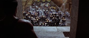 Movie still from “Judge Dredd” (1995), directed by Danny Cannon – A large group of people are gathered together in a parking lot; Extreme Wide shot, High angle