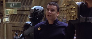 Movie still from “Judge Dredd” (1995), directed by Danny Cannon – A man standing next to another man wearing a helmet; Close Up shot, Over the shoulder angle