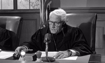 Movie still from “Judgment at Nuremberg” (1961), directed by Stanley Kramer – An older man in a court room wearing a robe and sitting at a desk; Medium shot, Low angle