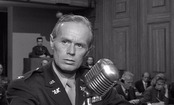 Movie still from “Judgment at Nuremberg” (1961), directed by Stanley Kramer – An old photo of a man in a military uniform holding a microphone in front of a group of people; Close Up shot, Over the shoulder angle