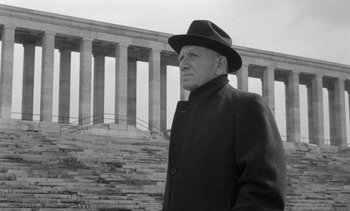 Movie still from “Judgment at Nuremberg” (1961), directed by Stanley Kramer – An older man wearing a hat and a coat standing in front of a building; Medium shot, Low angle