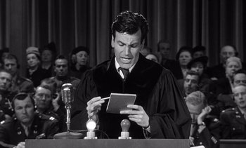Movie still from “Judgment at Nuremberg” (1961), directed by Stanley Kramer – A man wearing a robe and holding a book in front of a microphone; Medium shot, High angle