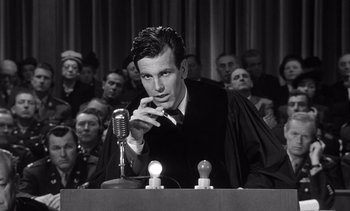 Movie still from “Judgment at Nuremberg” (1961), directed by Stanley Kramer – A man in a courtroom with a microphone and candles; Medium shot, Low angle