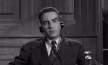 Movie still from “Judgment at Nuremberg” (1961), directed by Stanley Kramer – A man in a suit and tie with a microphone in his ear; Close Up shot, Low angle