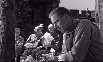 Movie still from “Judgment at Nuremberg” (1961), directed by Stanley Kramer – A group of men sitting on the side of a road; Medium shot, Over the shoulder angle