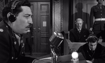 Movie still from “Judgment at Nuremberg” (1961), directed by Stanley Kramer – Two men are sitting at a table and one is on a microphone; Medium shot, Over the shoulder angle