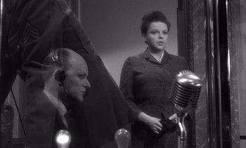 Movie still from “Judgment at Nuremberg” (1961), directed by Stanley Kramer – A woman standing next to a microphone in front of a man; Medium shot, Low angle